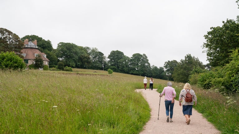 Walkers on a level path beside a meadow and with A la Ronde house in the background